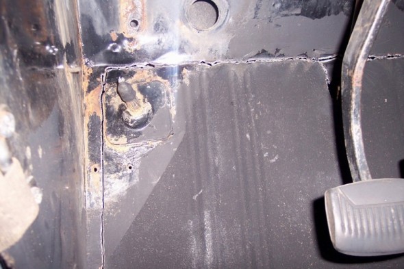close-up of rusty floor pan and brake pedal assembly inside a vehicle