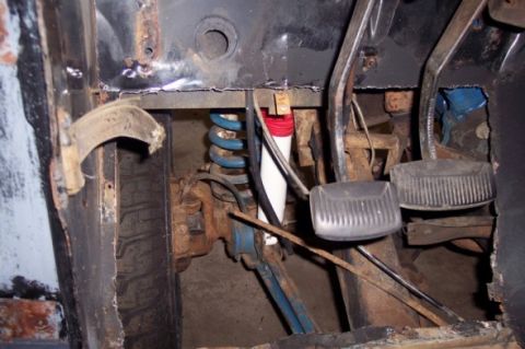 1976 Ford Bronco - The driver's side footwell shows significant rust and wear on the floor pan and pedals, with visible suspension parts.