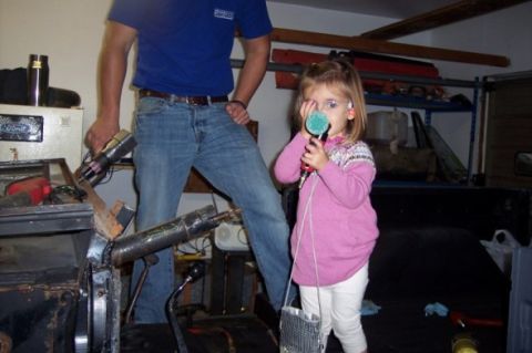 1976 Ford Bronco - A young girl holds a microphone in a garage, with a man and vehicle parts visible in the background.