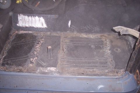 1976 Ford Bronco - The interior floor of a vehicle shows signs of rust and repair work, with a torn piece of fabric visible.