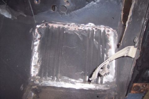 1976 Ford Bronco - Close-up view of a welded floor pan repair, showing metalwork and a seatbelt strap attached to the side.