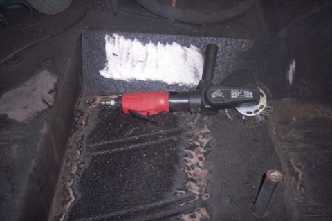 1976 Ford Bronco - An air-powered grinder with a wire wheel is used to clean rust from a vehicle's floor pan.