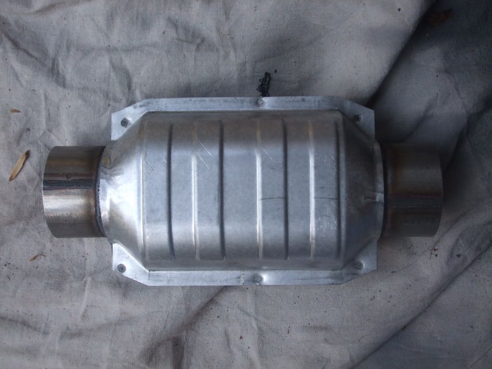 Catalytic converter with ribbed metal casing and two pipe ends, resting on a grey cloth