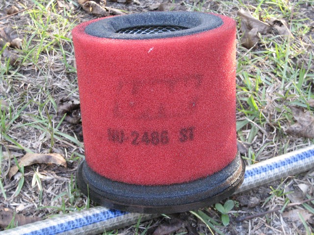 Red foam cylindrical air filter marked NU-2486 ST sitting on grass beside a hose