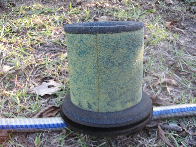 Cylindrical pleated air filter element with rubber caps on grass by a tape measure