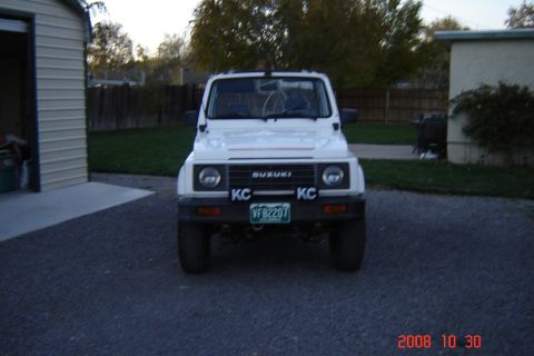 1988 Ford Bronco - A white Suzuki Samurai is parked in front of a garage and house.