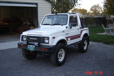 1988 Ford Bronco - A white Suzuki Samurai is parked in front of a garage.