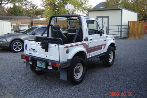 1988 Ford Bronco - A white Suzuki Samurai is parked in a gravel lot next to a dark-colored car.