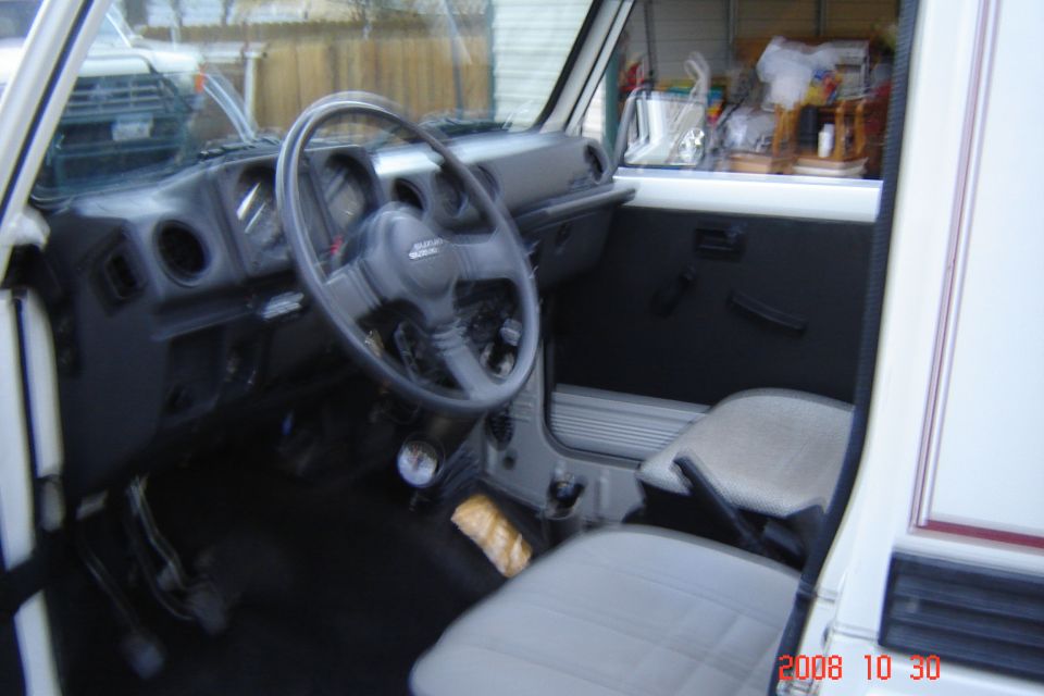 Suzuki Samurai dashboard, steering wheel, and seats. Text on steering wheel says SUZUKI