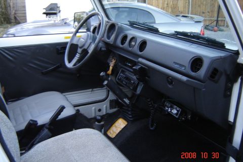 1988 Ford Bronco - The interior of a white Suzuki Samurai shows its dashboard, steering wheel, and seats. A CB radio is mounted below the dash.