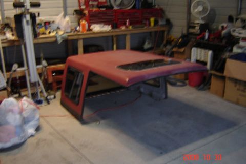 1988 Ford Bronco - A red truck cap with tinted windows is stored in a cluttered garage.