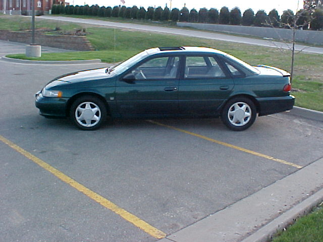 Dark green sedan parked in a lot, side view, sunroof, five-spoke wheels