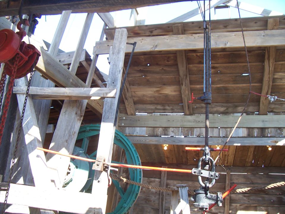 Wooden structure with a large green wheel, red hoist, and metal machinery