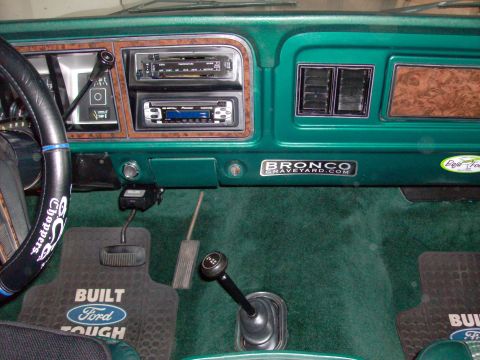 1978 Ford Bronco - Interior view of a 1978 Ford Bronco, green carpeting, woodgrain accents, and a "Bronco Graveyard" decal on the dashboard.