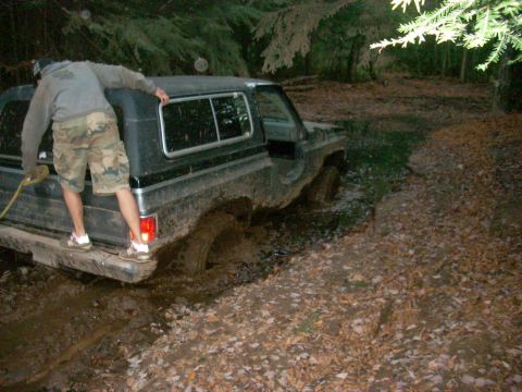1988 Chevrolet Blazer - A person stands on the bumper of a black 1988 Chevrolet Blazer as it is stuck deep in mud.