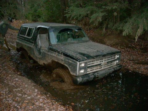 1988 Chevrolet Blazer - A 1988 Chevrolet Blazer is stuck in a muddy trail in the woods, with a person attempting to push it.