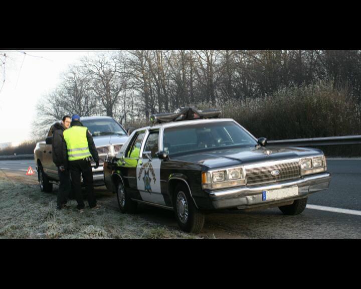 1991 Ford Crown Victoria police car parked next to a pickup truck with two men standing by