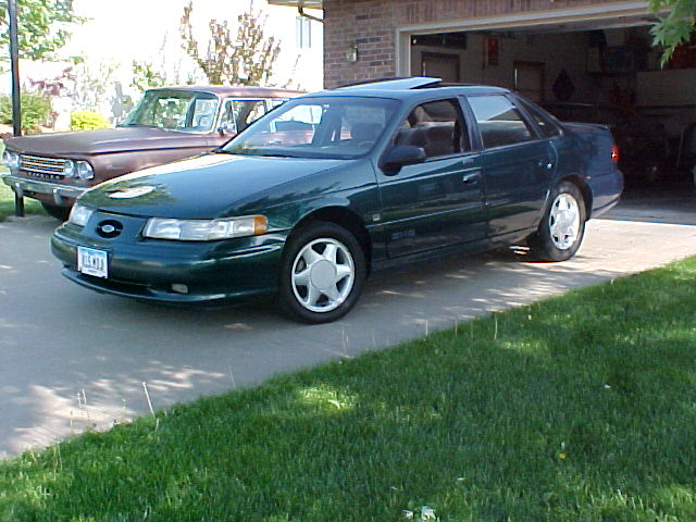 Green sedan parked in front of a garage, with an older brown car to its left