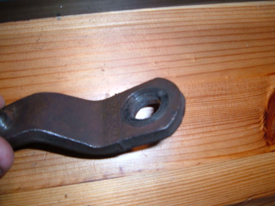 Bare steel clutch release lever with welded bushing eye held over a wood board