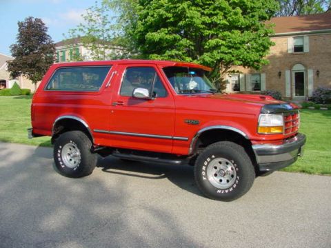 1992 Ford Bronco - A red 1992 Ford Bronco is shown from the front passenger side, parked in front of a residential building.