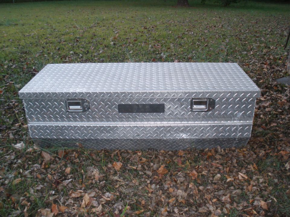 Diamond plate truck bed toolbox with two handles and a black rectangular panel on the front