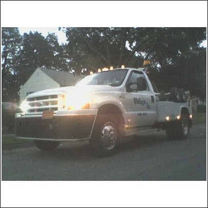 1990 Ford Bronco - A white tow truck is parked on a street with its lights illuminated.