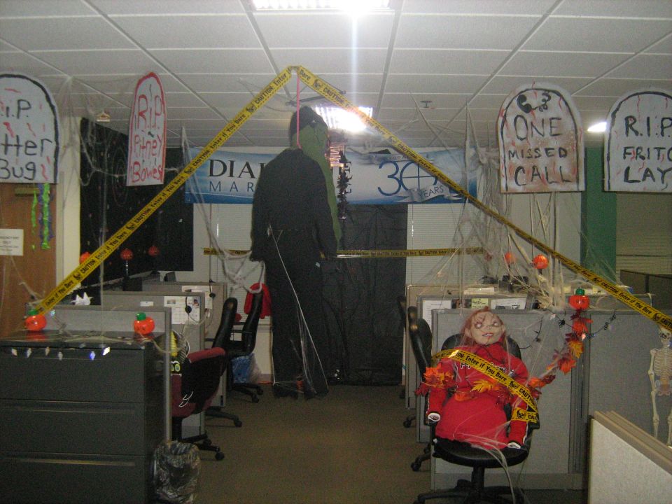 Office cubicles decorated for Halloween with caution tape and tombstone cutouts