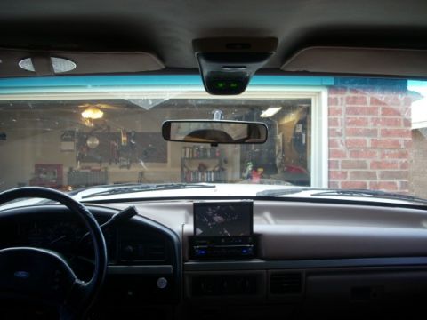 1992 Ford Bronco - The dashboard of a vehicle shows an aftermarket stereo system and a rearview mirror, with a garage visible through the windshield.