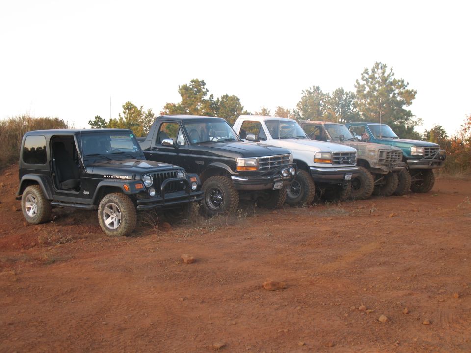 Black Jeep Wrangler Rubicon and Ford trucks parked on red dirt