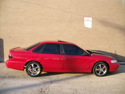 1993 Ford Taurus - Side view of a red 1993 Ford Taurus sedan with aftermarket wheels.