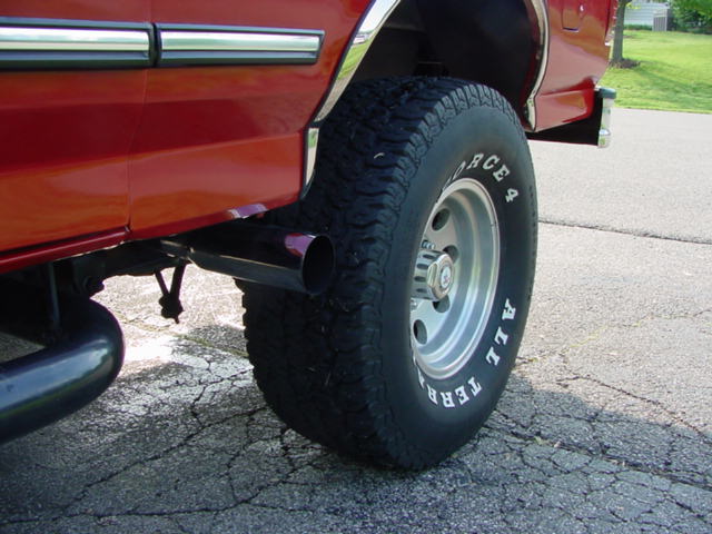 Chrome exhaust tip ahead of rear wheel on red Ford truck with BFGoodrich All-Terrain tire