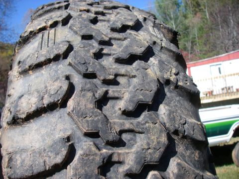 1978 Ford Bronco - This image focuses on the aggressive tread pattern of an off-road tire, with a portion of a vehicle visible in the background.