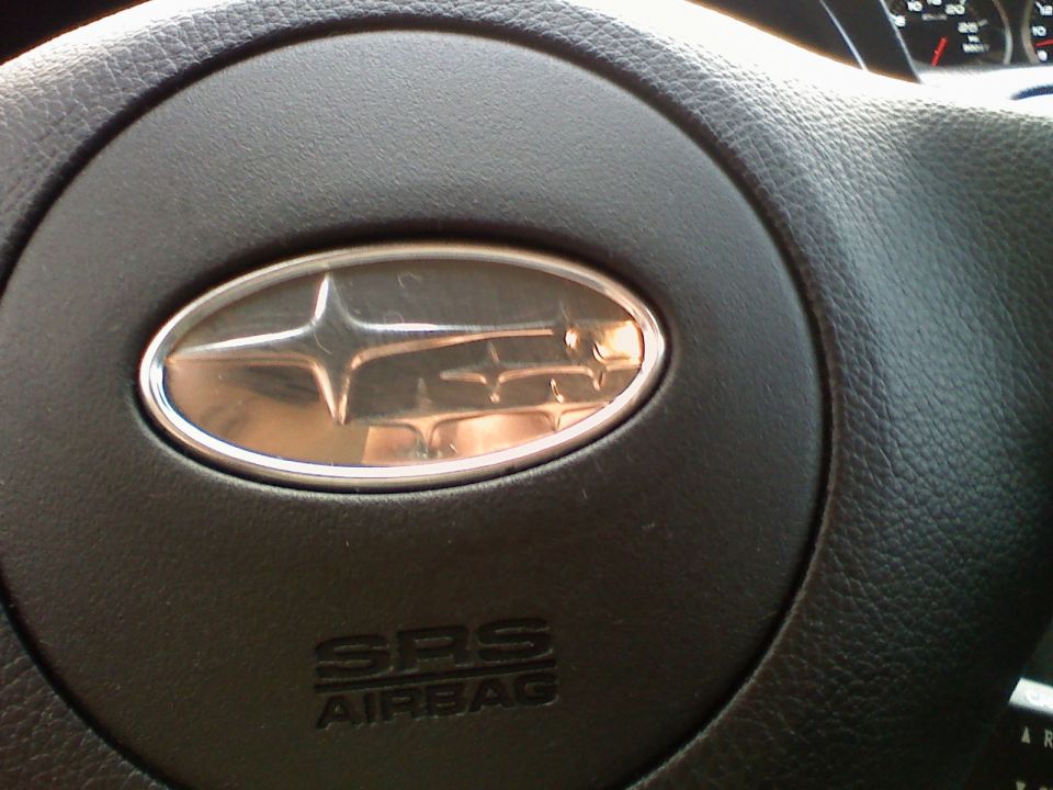 Chrome Subaru star emblem on a black steering wheel airbag cover marked SRS AIRBAG