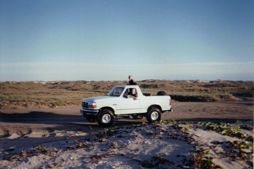White 1992 Ford Bronco on a sandy road near dunes