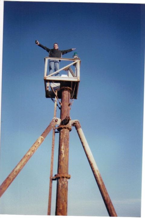 1992 Ford Bronco - A person stands in a metal cage atop a rusty structure against a clear blue sky.