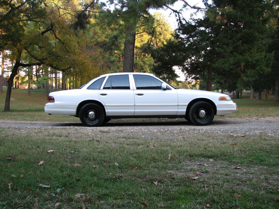 White sedan with black wheels parked on a gravel road, side view