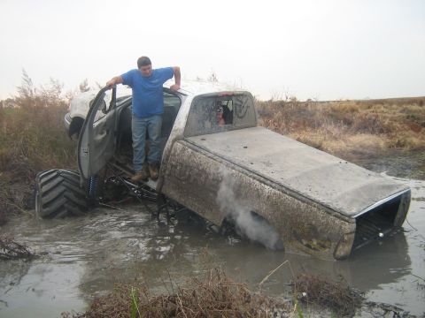 2004 Acura TL - A monster truck is stuck in a muddy area, with a person standing in the driver's side door.