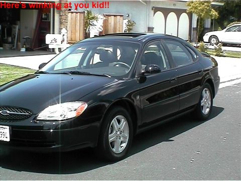 2002 Ford Taurus - A black sedan is parked on an asphalt surface in front of a house.