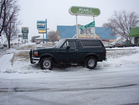 1993 Ford Bronco - A 1993 Ford Bronco sits parked on a snow-covered street with commercial buildings in the background.