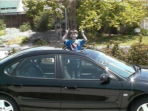 2002 Ford Taurus - Child pops out of the sunroof of a black 2002 Ford Taurus.
