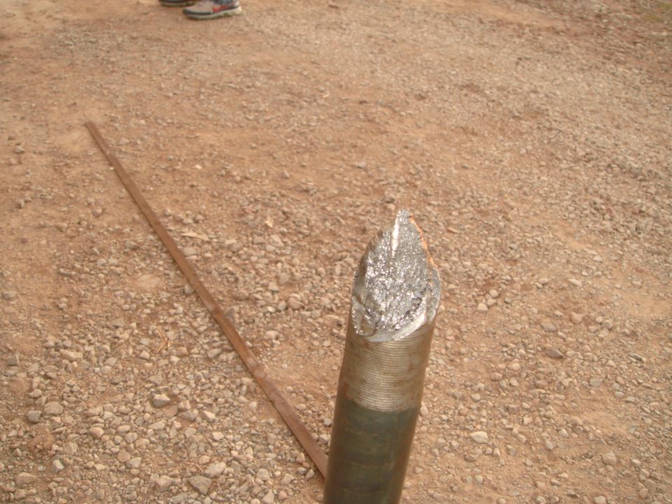 metal drill bit with threaded shaft on gravel ground