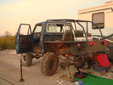 1992 Ford Bronco - A blue off-road truck is being worked on, with its rear axle lifted and a person attending to it.