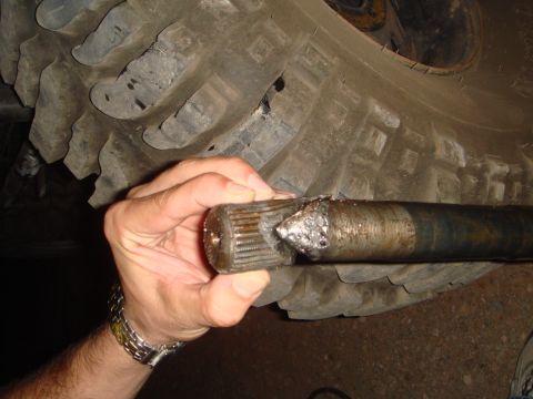 1992 Ford Bronco - Broken axle shaft being held up, with a large tire tread visible in the background.