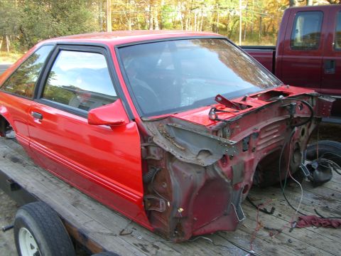 1988 Ford Bronco - A red car body, possibly a 1987 Ford Mustang, is seen on a trailer with its front end removed.