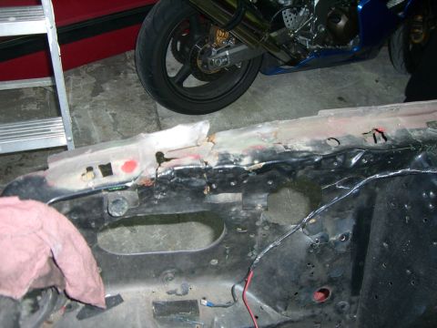 1988 Ford Bronco - Close-up of a damaged vehicle frame, with a motorcycle and ladder visible in the background.