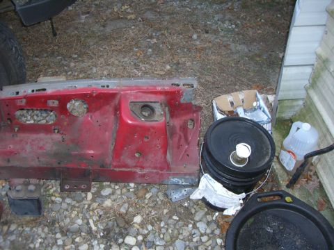 1988 Ford Bronco - A red metal car part is seen on the ground next to various containers and a tire.