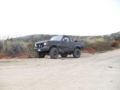 1990 Ford Bronco - This lifted truck, likely from the late 1980s, is parked off-road.