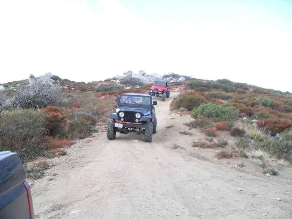Two Jeeps driving up a dirt road in a hilly, arid landscape