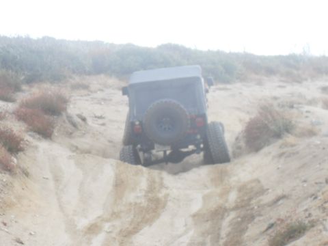 1990 Ford Bronco - A black Jeep Wrangler navigates a sandy off-road trail from a rear perspective.