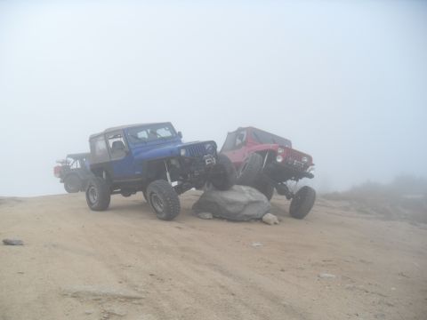 1990 Ford Bronco - Two off-road Jeeps navigate a rocky incline on a foggy day.